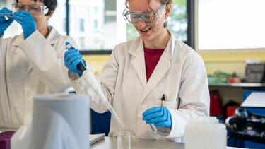 Students taking water samples from a beaker.