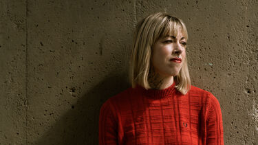Helen Mort against a wall wearing an orange jumper 
