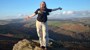 A woman stands on a rock, overlooking a vally