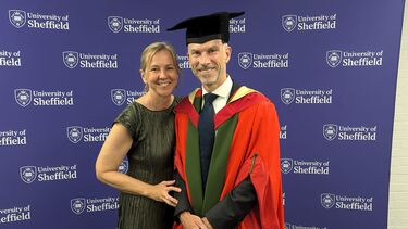 Blonde woman in a smart black dress, with a man wearing a red graduation cap and gown