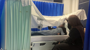 Student midwives drape a bedsheet over a hospital bed