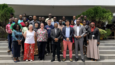 A group photo of people standing on the steps outside a white building (under a sign for the college of Basic and Applied Sciences at the University of Ghana)