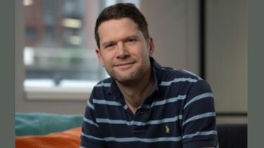 Professional headshot of Jonathan looking at camera sitting on chair