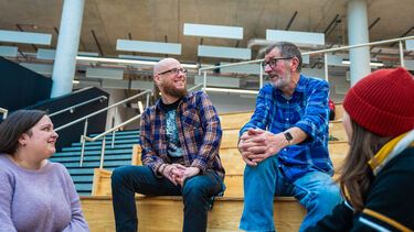 Four mature students from the University of Sheffield's Department for Lifelong Learning sitting on the wooden steps inside the Wave having a happy conversation