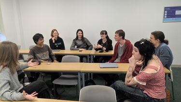 A group of 8 students sitting in a circle talking and smiling