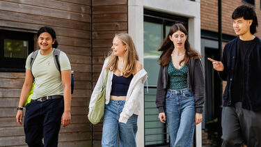 Four students walking along a path in front of a student accommodation building