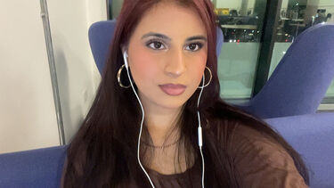 Asmaa has long dark hair and sits on a blue sofa.