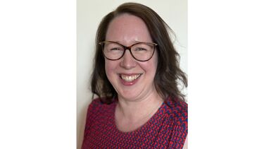 Person smiling, with brown hair and glasses, wearing a blue and red top.