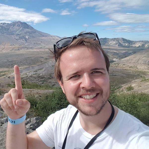 Profile picture of Tom Pering pointing at Mount St Helens volcano in USA