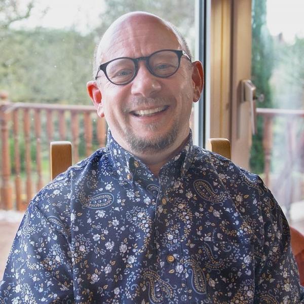 Profile picture of Man with glasses smiling at camera sitting on a chair