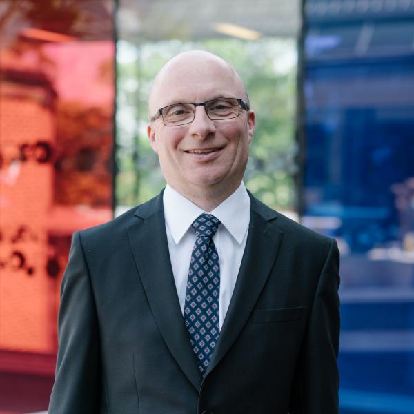 Profile picture of Andrew Smith wearing a white shirt, blue patterned tie and black jacket.