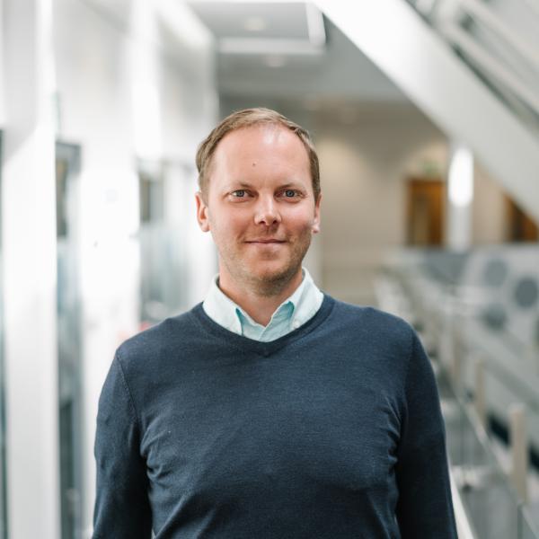 Profile picture of Stephen Allen, stood on the mezzanine walkway, wearing a dark blue jumper and light blue shirt.