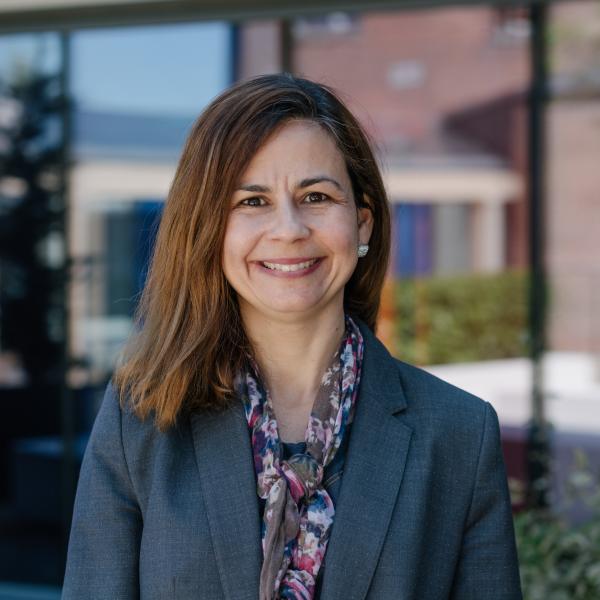 Profile picture of Juliana Meira wearing a dark blazer and colourful scarf.