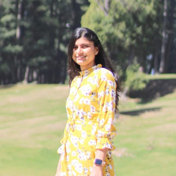 Profile picture of Shriya Bajaj standing on a green field in a yellow dress with trees in the background