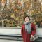 Alumni Xin Feng standing in front of a tree and a building