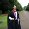 A graduating student wearing a graduation gown and holding his gap.