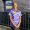 Catherine Nakawunde wearing hospital scrubs outside a brick building and iron fence