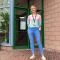 Amy Harding wears a pastel ombre jumper and skinny blue jeans. She has blonde hair. She stands in front of a glass panelled building.