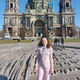 A female student stands outdoors with a large historical building and blue sky behind them. They are smiling at the camera.