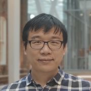 Image of asian man with dark hair and glasses wearing blue checked shirt. He is smiling at the camera.