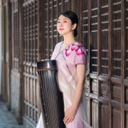 Profile picture of Shu Jiang holding her instrument in a white and purple dress. 