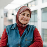 A headshot of Ghada Sasi wearing a red jumper underneath a blue denim waistcoat