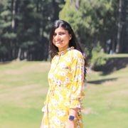 Shriya Bajaj standing on a green field in a yellow dress with trees in the background