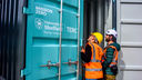 two men in hard hats and hi-vis vests stand outside a blue and grey shipping container - the direct air capture plant - with the mission zero and uni of sheffield logos printed on