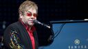 Elton John sits at a Yamaha piano and sings into a microphone