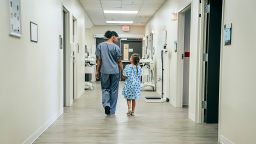 A photograph of a nurse walking with a child down a hospital corridor.