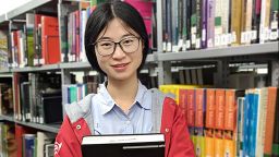 Yue Cai stood in front of a bookshelf smiling