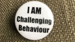 A pin badge reading 'I AM challenging behaviour' 