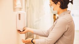 A picture of a woman using a hand sanitiser dispenser in a workplace environment.