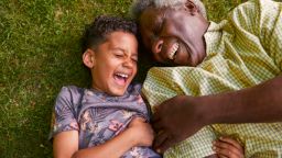Grandson and grandfather laughing while laying on grass