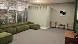 A photograph inside a room, with a large green sofa, chairs and a small table. Out of view is a projector screen. The wall is decorated to resemble the Sheffield Botanical Gardens,
