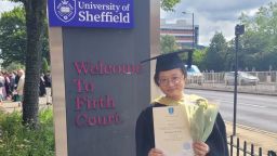 Mengzi Li in cap and gown holding her graduation certificate