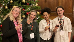 Scarlett, Kaydian, Rose and Arran stood holding wine glasses in front of a christmas tree