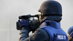 A journalist with a camera wearing a bullet-proof vest and helmet