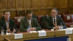 Three people sat desks in a parliamentary committee meeting