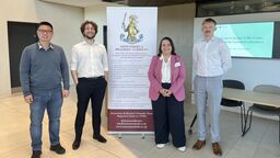 Three researchers stand in front of a pull up banner