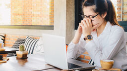 A person looking sad while looking at a laptop screen in a cafe.