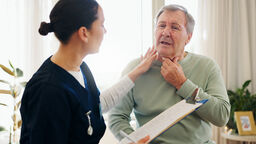 A doctor checking a patients neck while holding a clipboard.