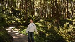 A female student stands on a path in a woodland and smiles towards the camera.