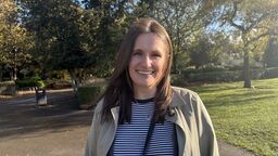 A person smiling at the camera with trees in the background.